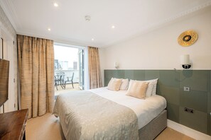 A hotel room with a large bed, a desk, a chair, and a view of the city through the window. - Fountain House (London)