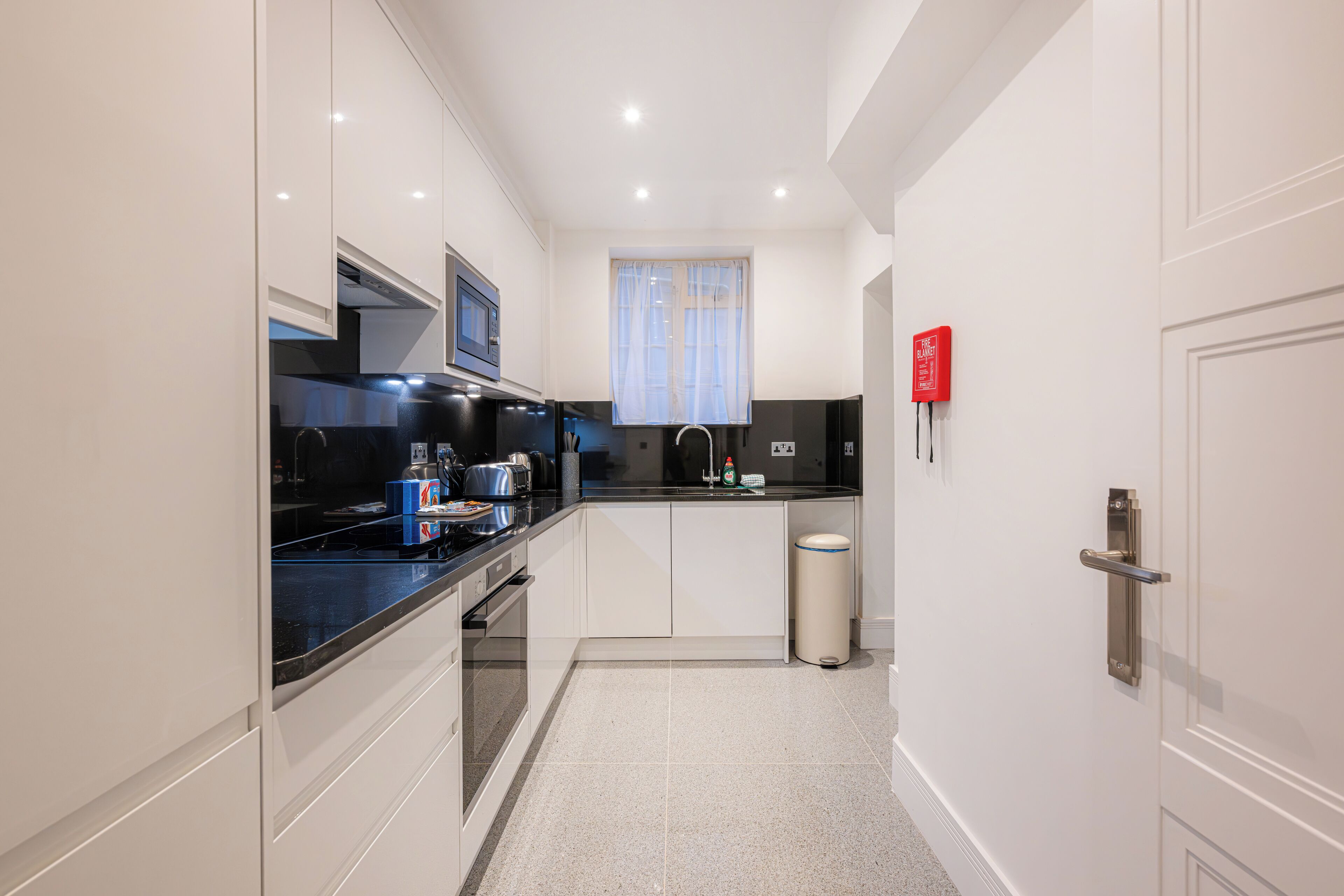 A modern kitchen with white cabinets, a black countertop, and a stainless steel sink.
