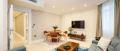 A modern living room with a sofa, coffee table, dining table, and TV.