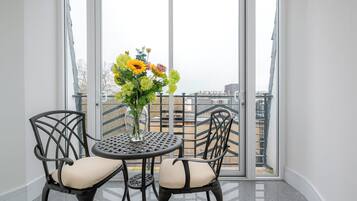 En balkon med et bord og stole, en vase med blomster og udsigt til bygninger.