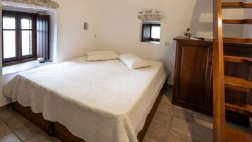 A bedroom with a large bed, a wooden wardrobe, a window, and a small mirror.
