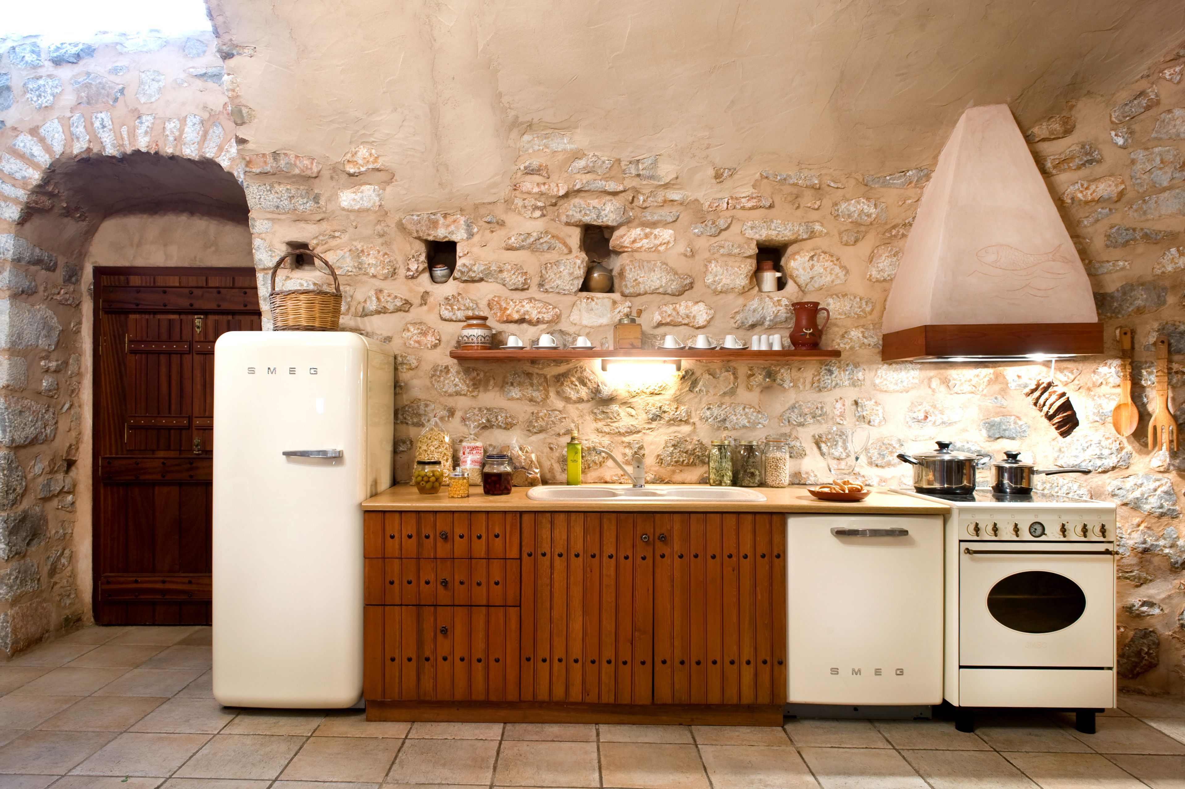 Una cocina con pared de piedra, armarios de madera, un refrigerador blanco, una estufa y diversos utensilios de cocina.