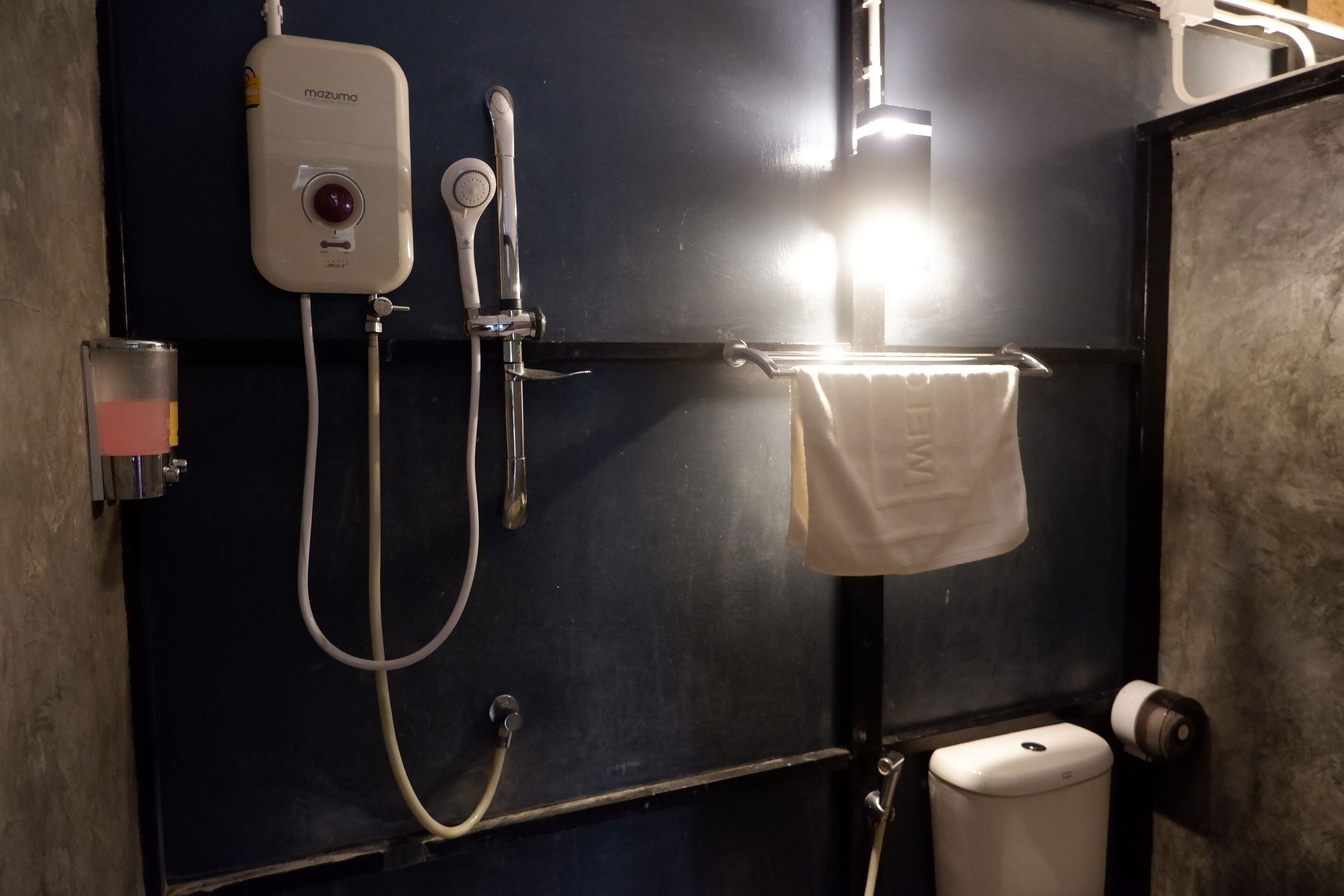 Un baño con pared negra, toallero blanco, inodoro y cabina de ducha con panel de control.