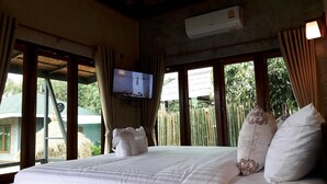 Una habitación de hotel con cama, cortinas, televisión y vistas al exterior.