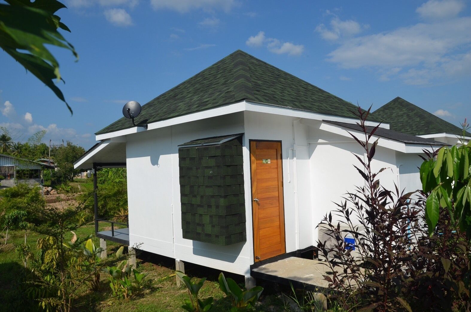 A small, single-story house with a green roof, a wooden door, and a satellite dish on the roof.