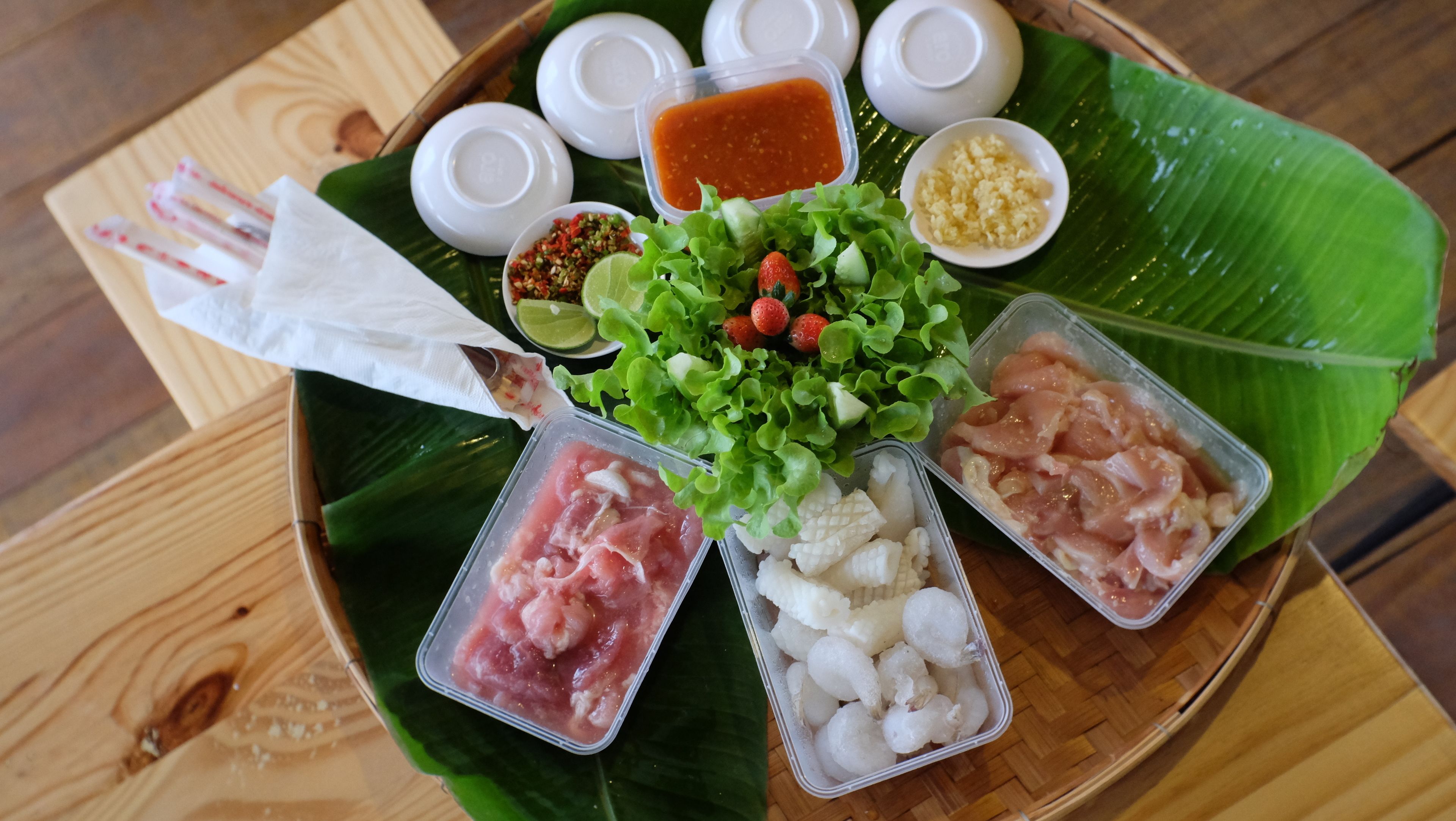 A tray with various food items including meat, vegetables, and condiments on a wooden table.