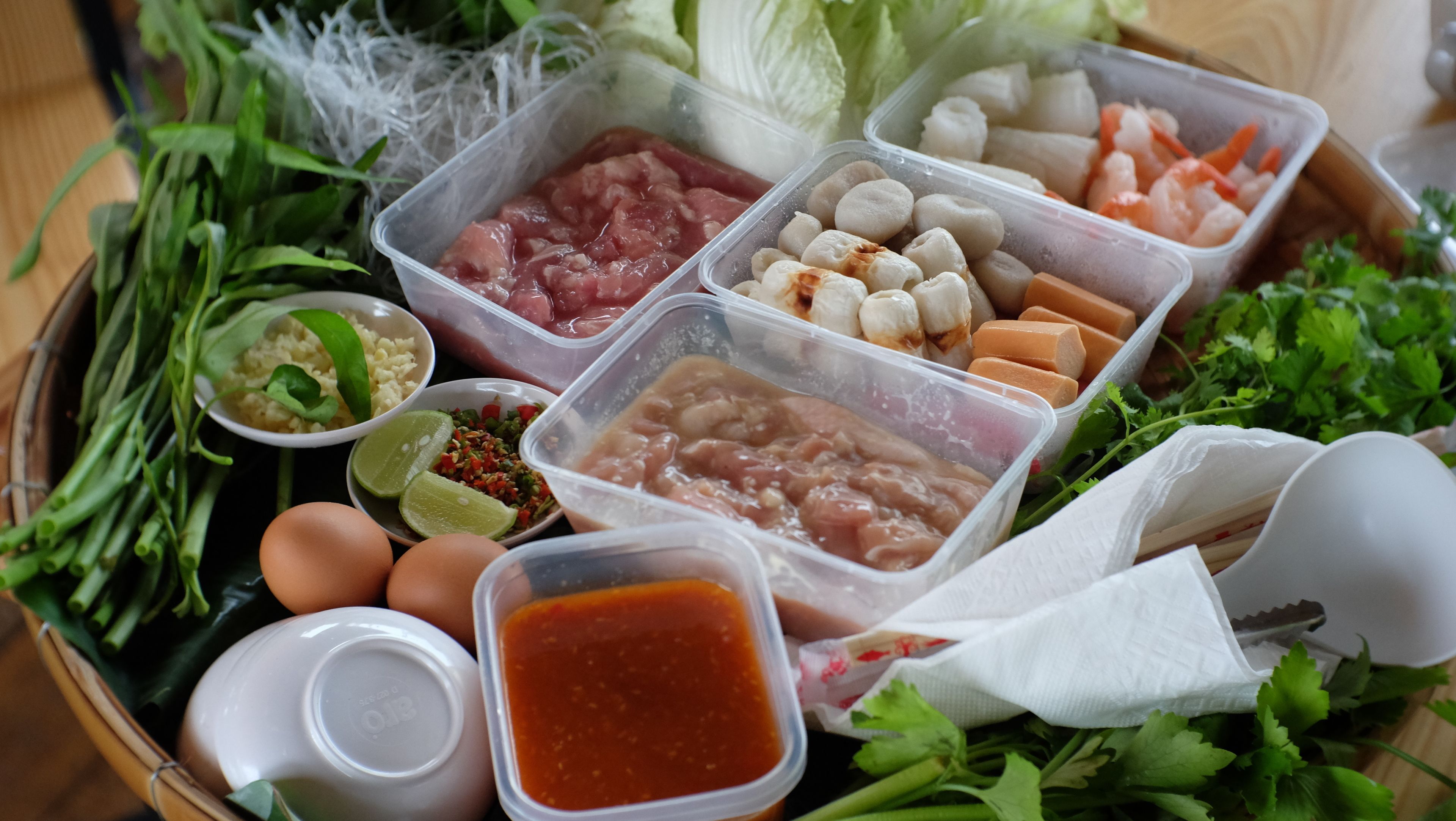 A variety of fresh ingredients and condiments, including meats, vegetables, and spices, arranged on a tray.