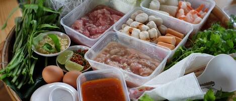 Eine Auswahl frischer Zutaten und Gewürze, darunter Fleisch, Gemüse und Kräuter, auf einem Tablett angerichtet.