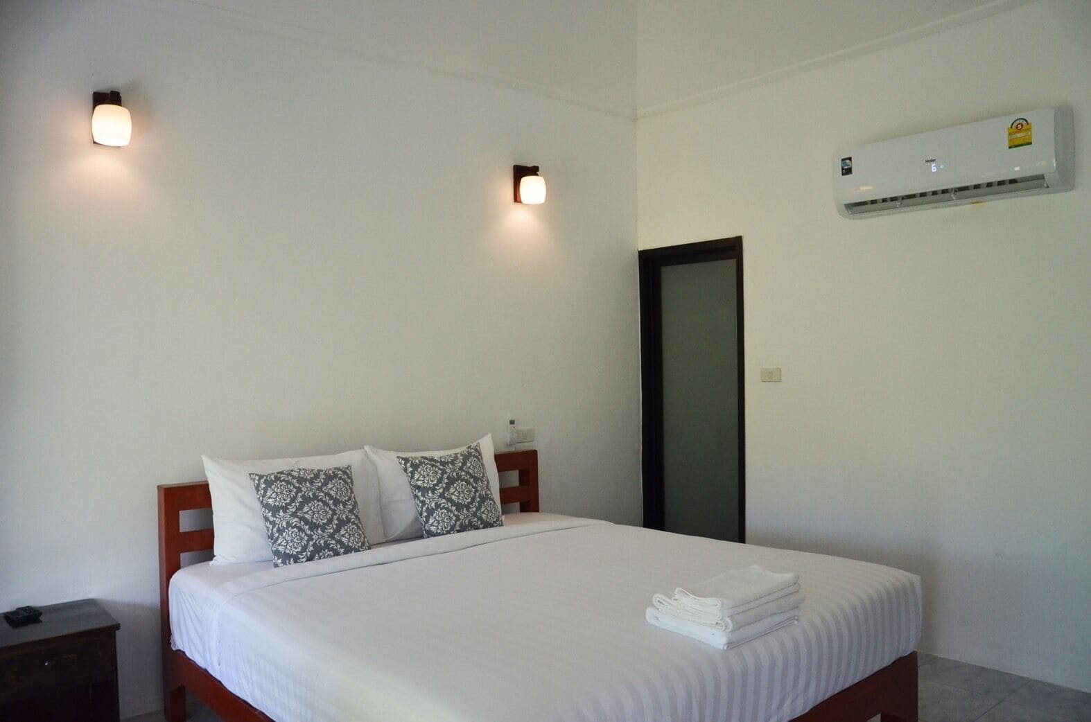 A bedroom with a bed, two bedside lamps, a wall-mounted air conditioner, and a door.