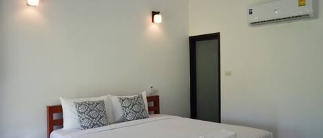 A bedroom with a bed, two bedside lamps, a wall-mounted air conditioner, and a door.