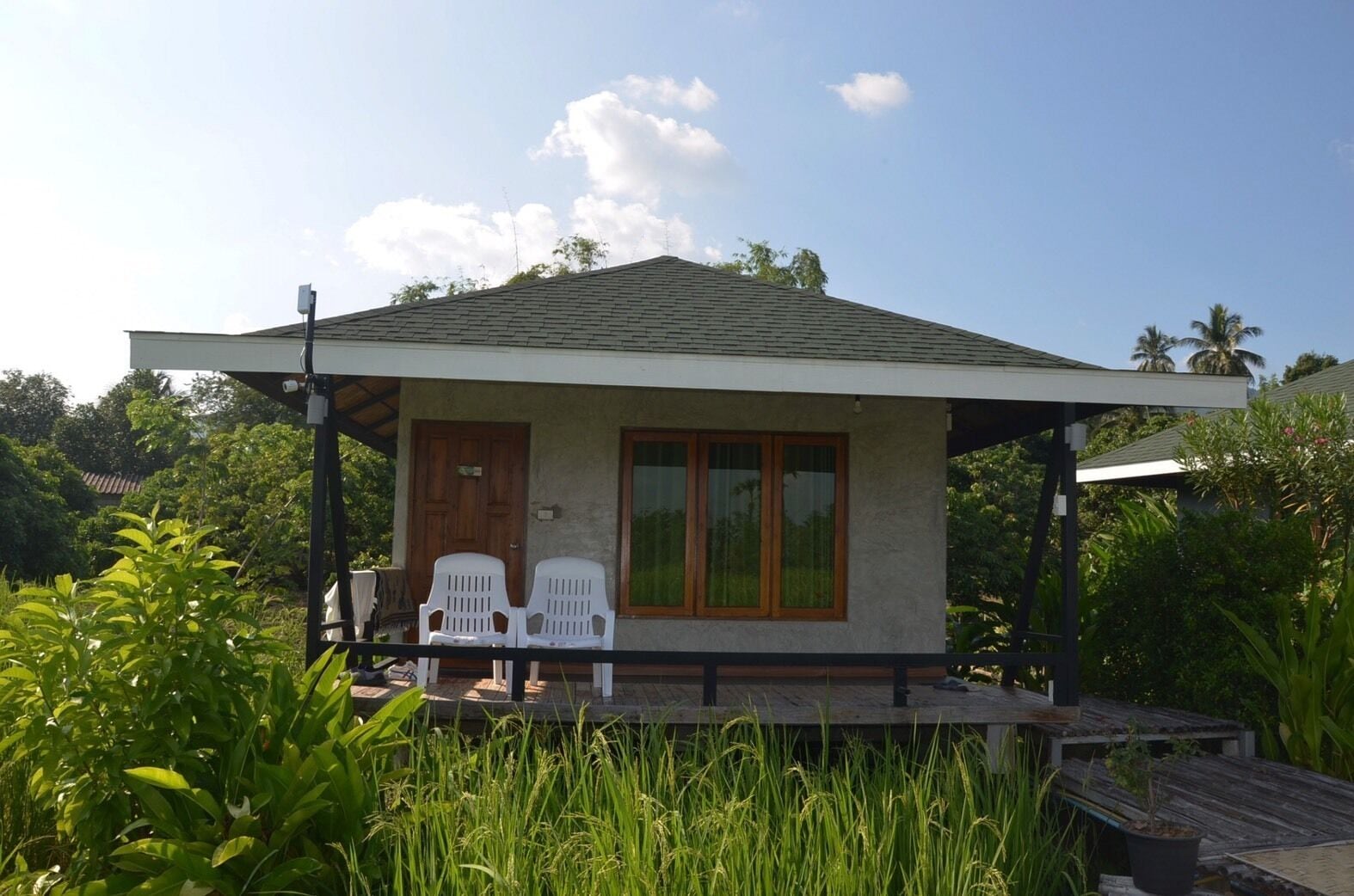 A small, single-story house with a porch, two white plastic chairs, and a wooden door.
