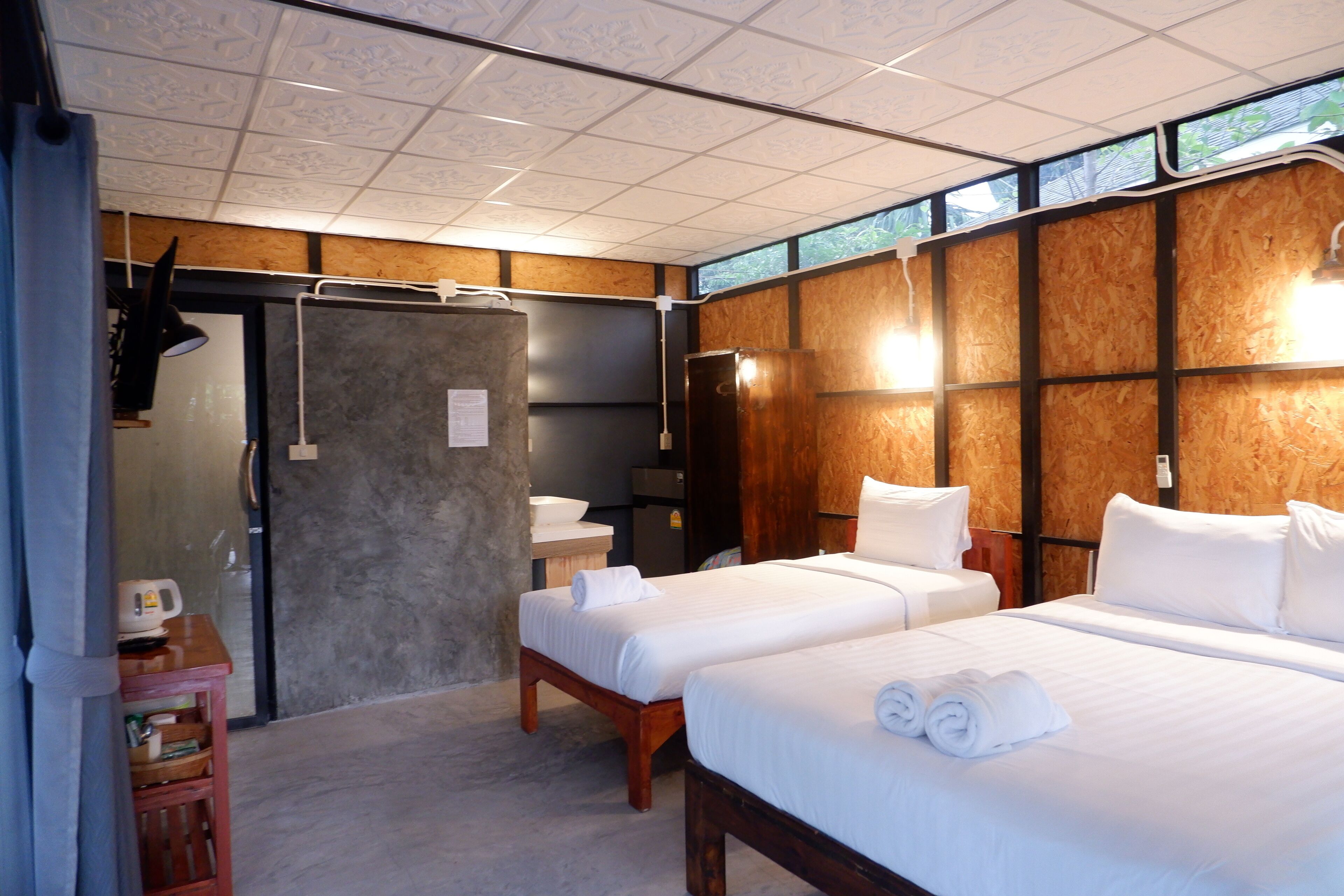 Une chambre d’hôtel avec deux lits, une tête de lit en bois, une petite salle de bain et une vue par la fenêtre.