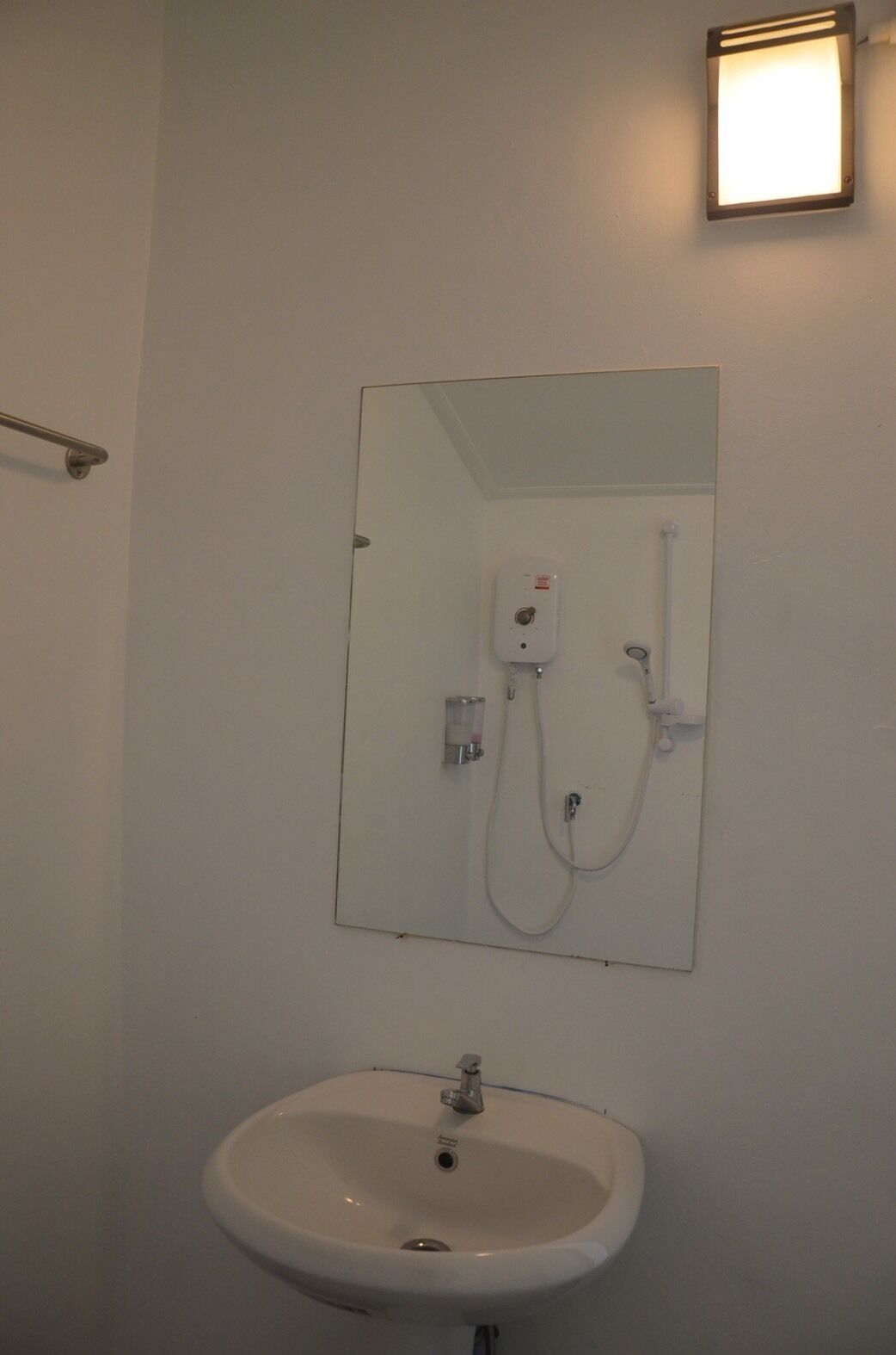 Een badkamer met een wit wastafel, een spiegel en een douche met een handdouche.