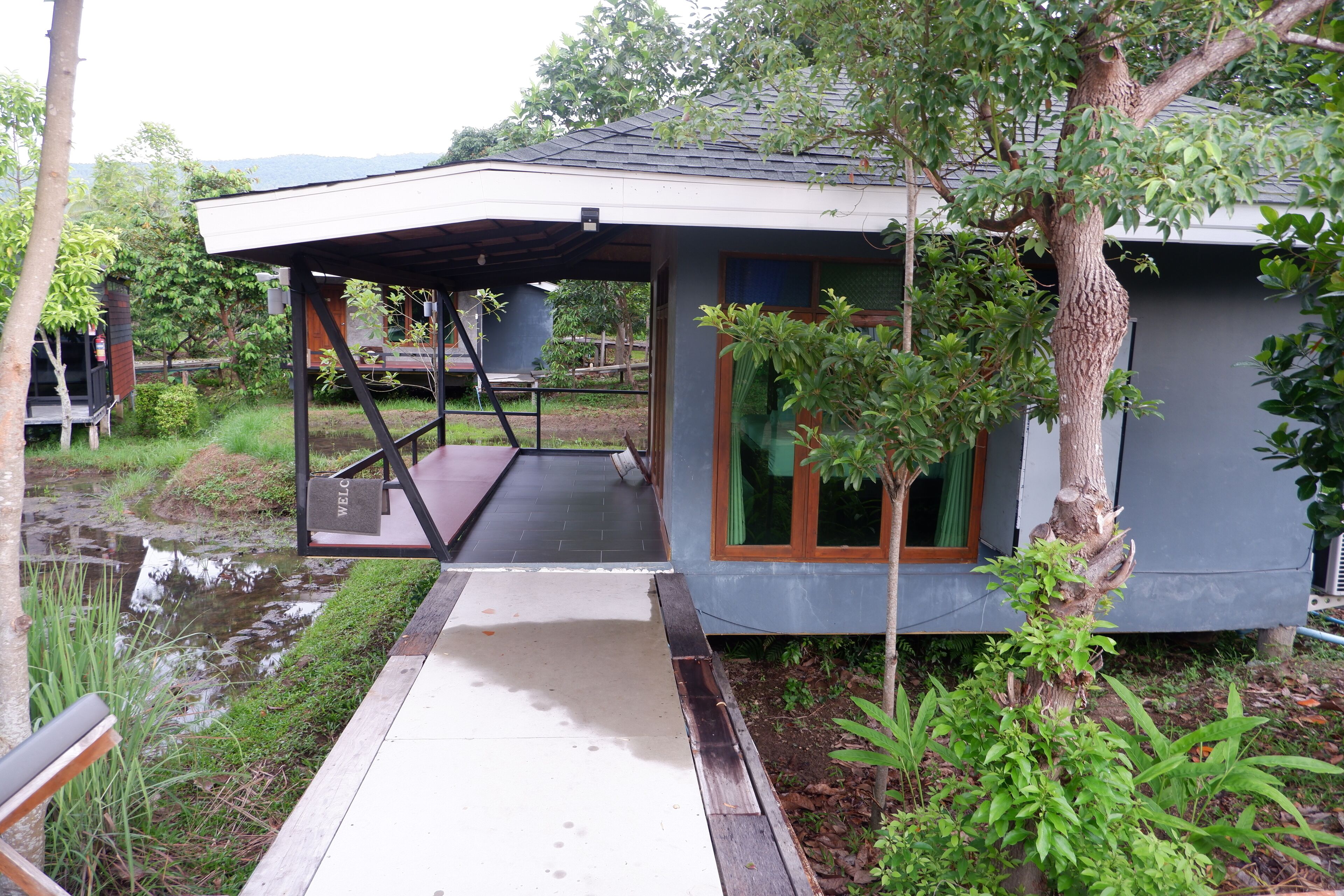 Una casa moderna con un porche cubierto, un pequeño estanque y abundante vegetación.