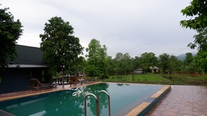 Una piscina con borde de baldosas, rodeada de árboles y un césped.