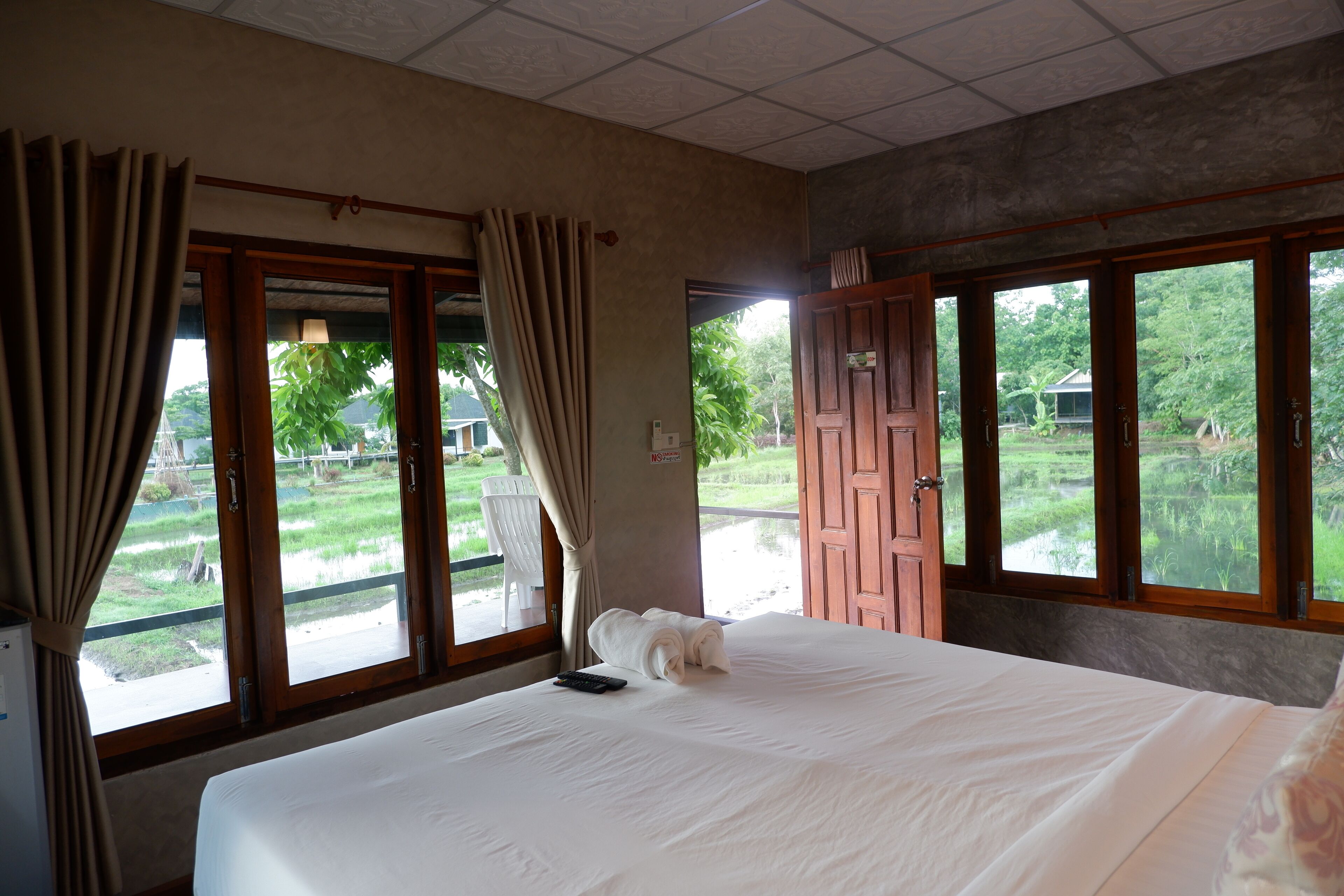 Une chambre d’hôtel avec un lit, une télécommande et une vue sur un jardin, grâce à de grandes fenêtres.