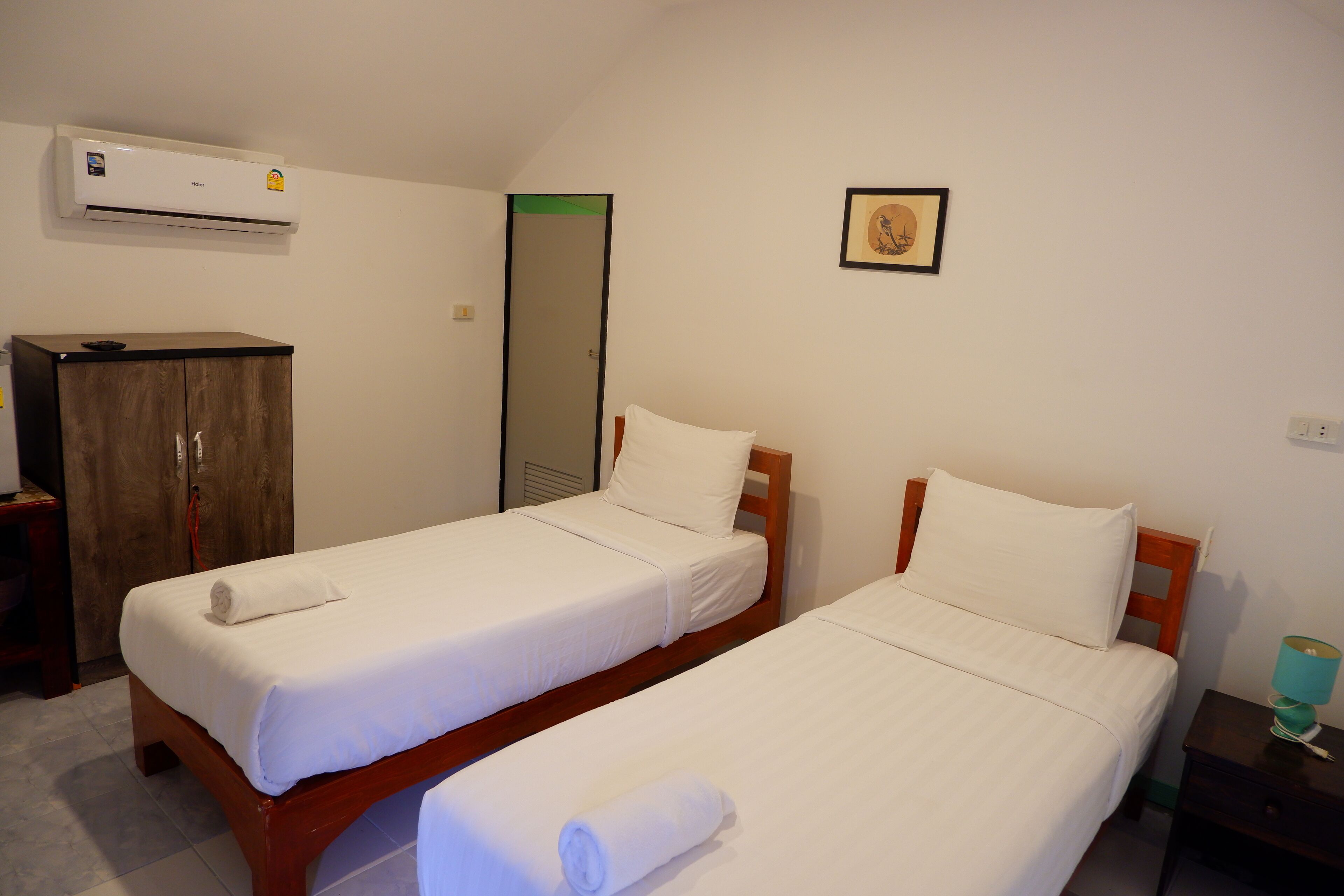 Dos camas individuales con estructura de madera y ropa de cama blanca, un armario de madera, un espejo y un aire acondicionado instalado en la pared.