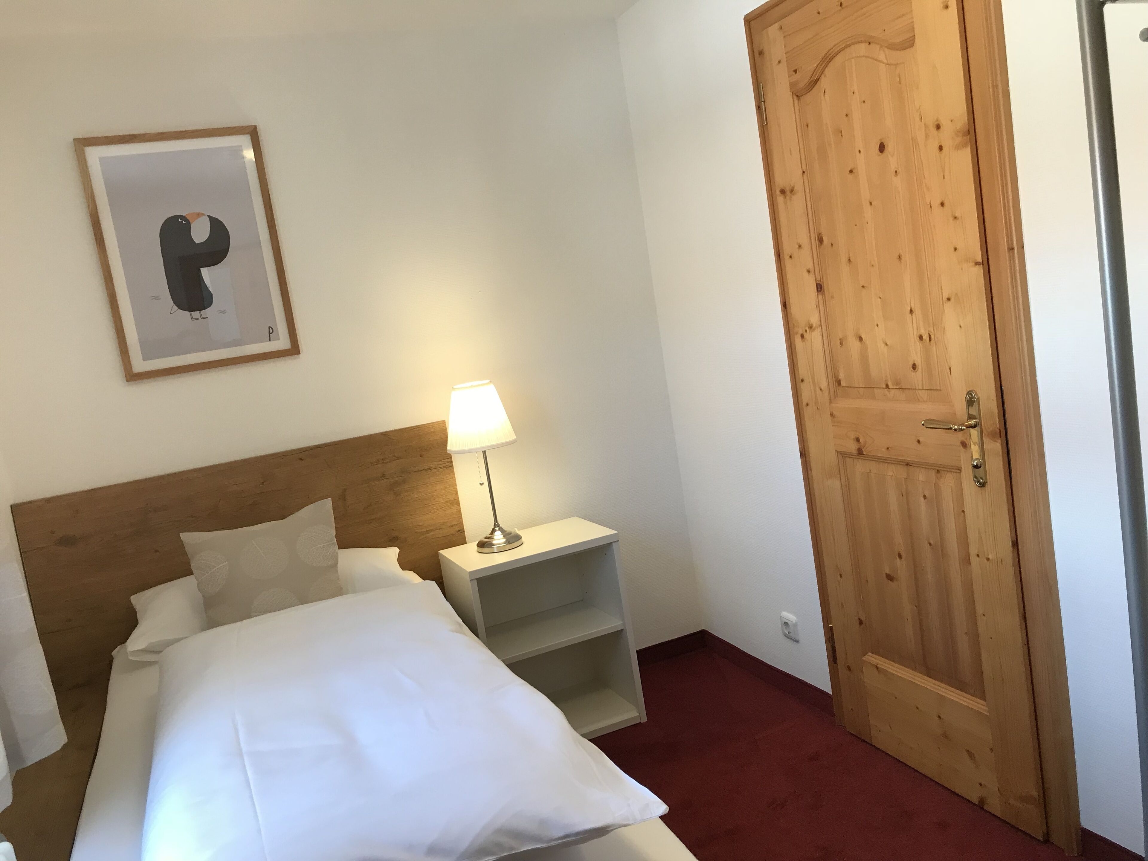 Une chambre d’hôtel avec une tête de lit en bois, une table de chevet avec une lampe, un tableau encadré au mur et une porte en bois.