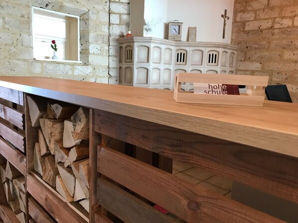 A wooden counter with a sign reading "hohe schule" and a rustic interior with a brick wall and a white cabinet with a cross.