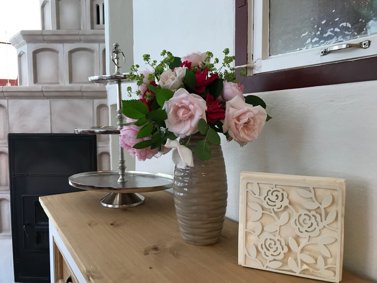 A wooden table with a vase of flowers, a cake stand, and a decorative panel.