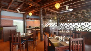 Een restaurant met houten tafels en stoelen, een bakstenen muur en uitzicht door een traliesraam.