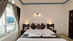 Een hotelkamer met een bed, twee nachtkastjes, gordijnen en uitzicht op de zee.