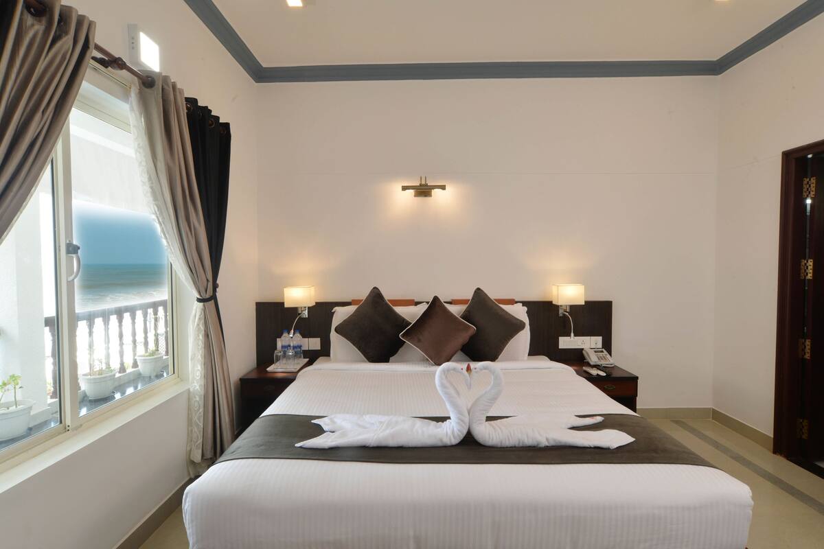 Una habitación de hotel con cama, dos mesitas de noche, cortinas y vista al mar.