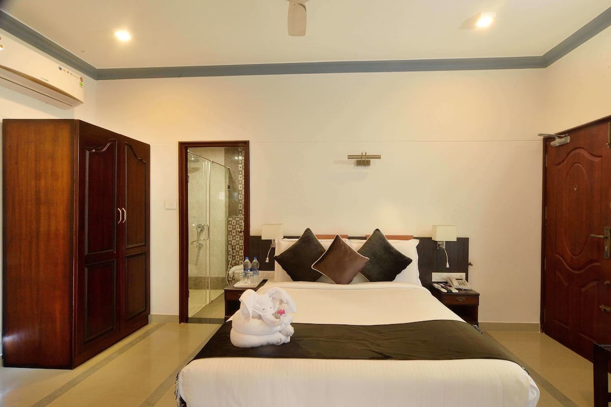 Habitación de hotel con una cama grande, un armario, baño con ducha y un escritorio con lámpara.