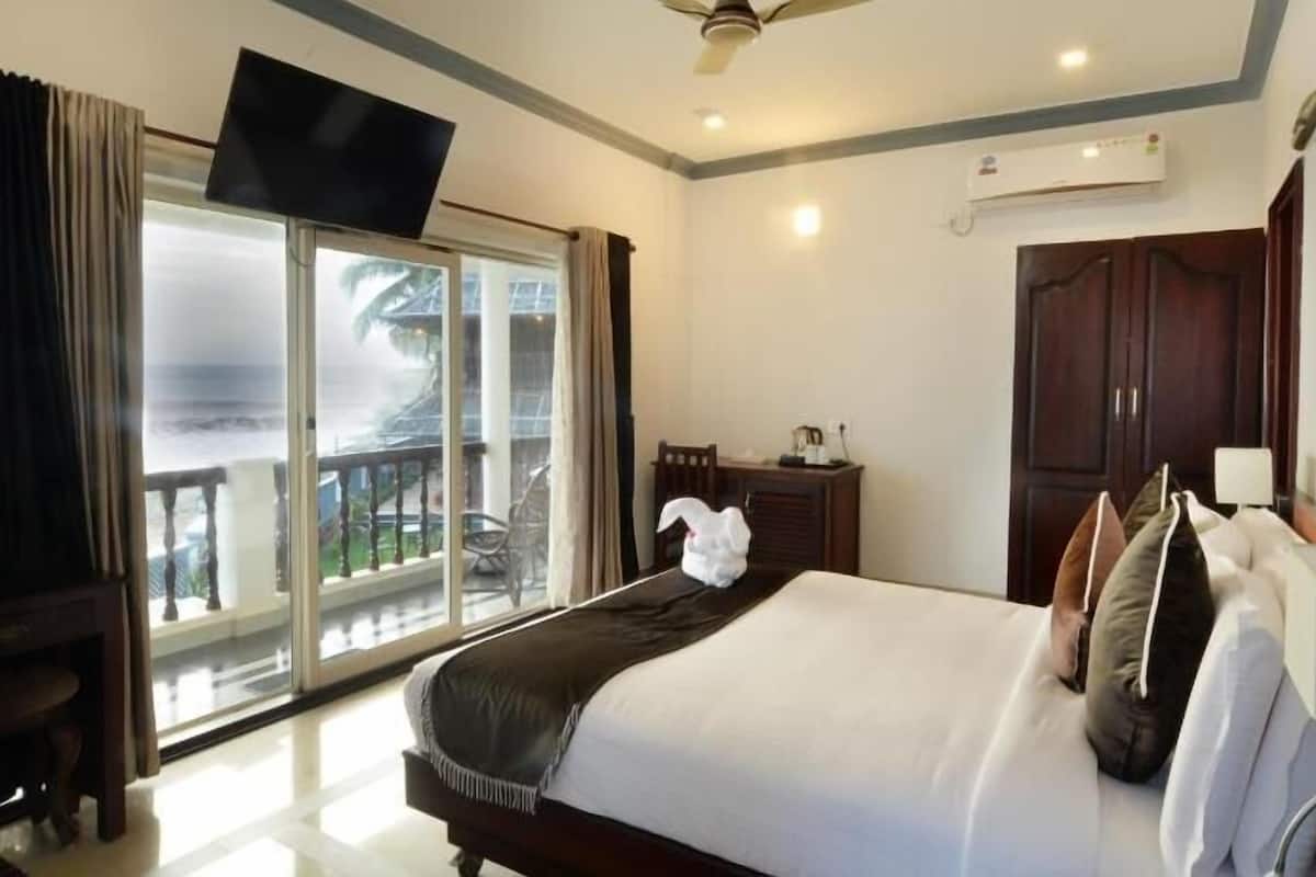 Una habitación de hotel con cama, escritorio, silla, televisión y balcón con vistas.