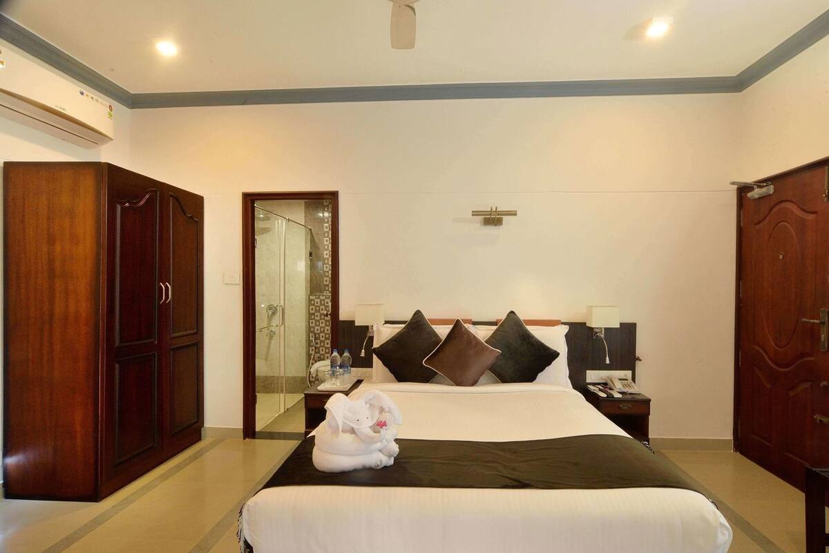 Habitación de hotel con cama, armario, espejo, mesita de noche y ducha.