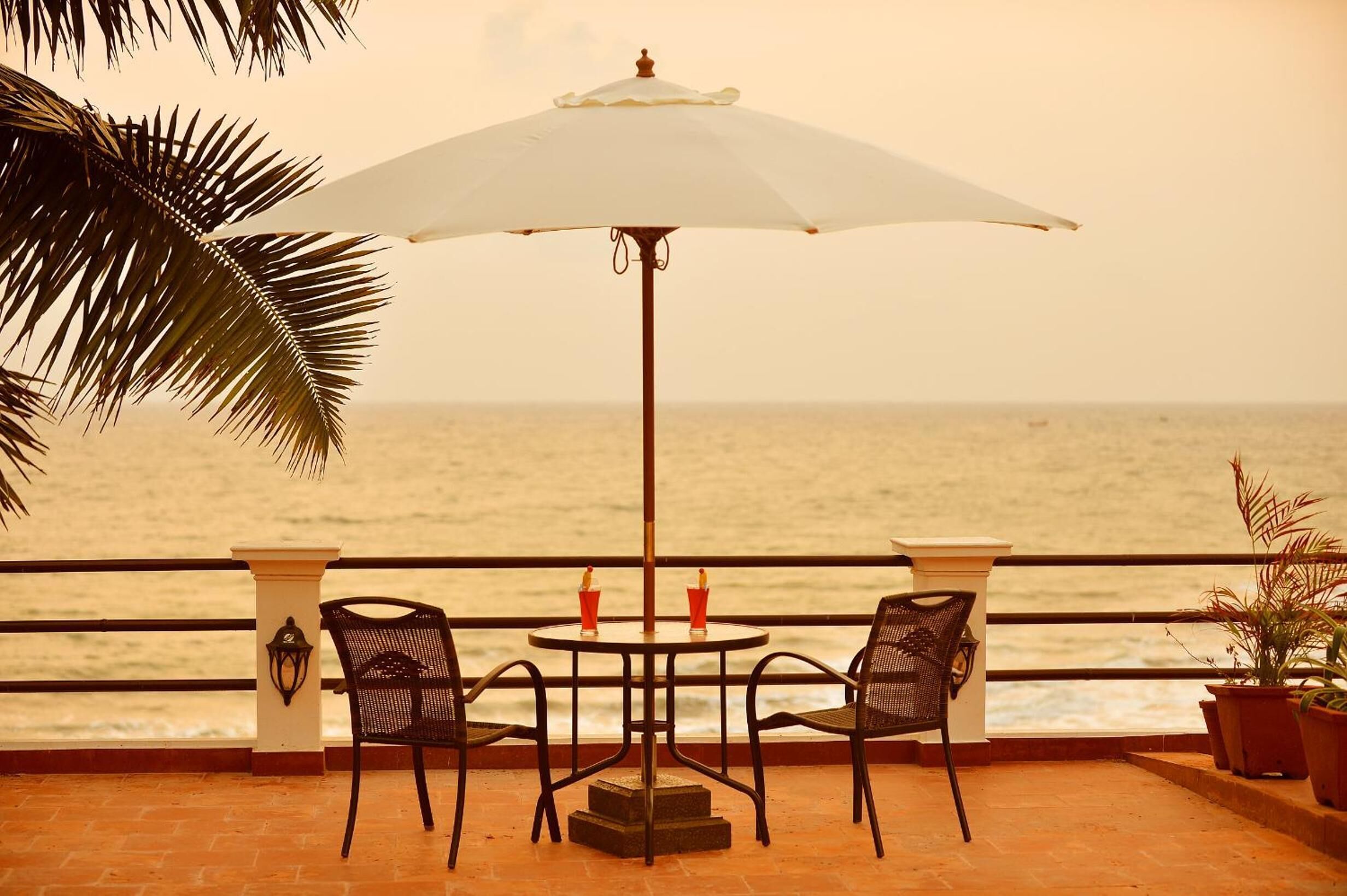 A table with two chairs and a white umbrella on a terrace overlooking the sea.
