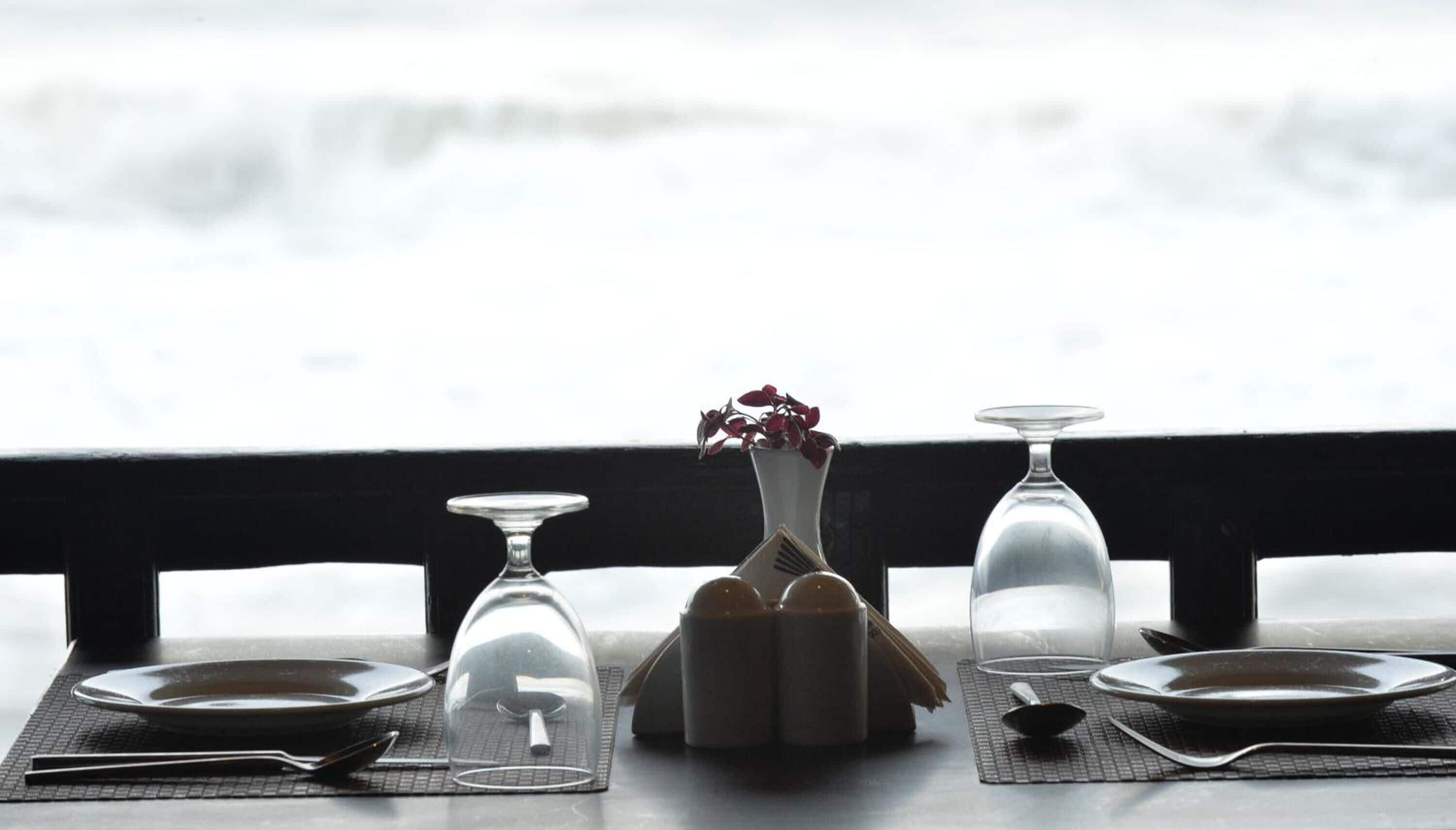 A dining table set with plates, cutlery, and a vase with red flowers.