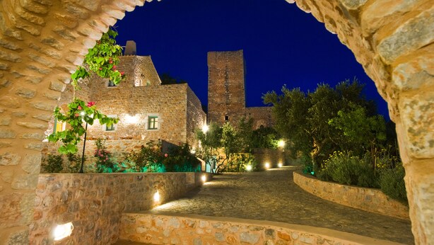 Un edificio de piedra con una torre, rodeado de follaje e iluminado por luces.