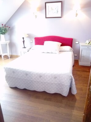 Une chambre à coucher avec un grand lit, une tête de lit rouge, une table de chevet avec une lampe et une petite armoire.