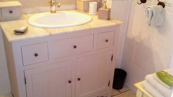 A bathroom with a white sink, vanity, and a mirror. There is a towel rack with a towel and a small potted plant on the vanity.