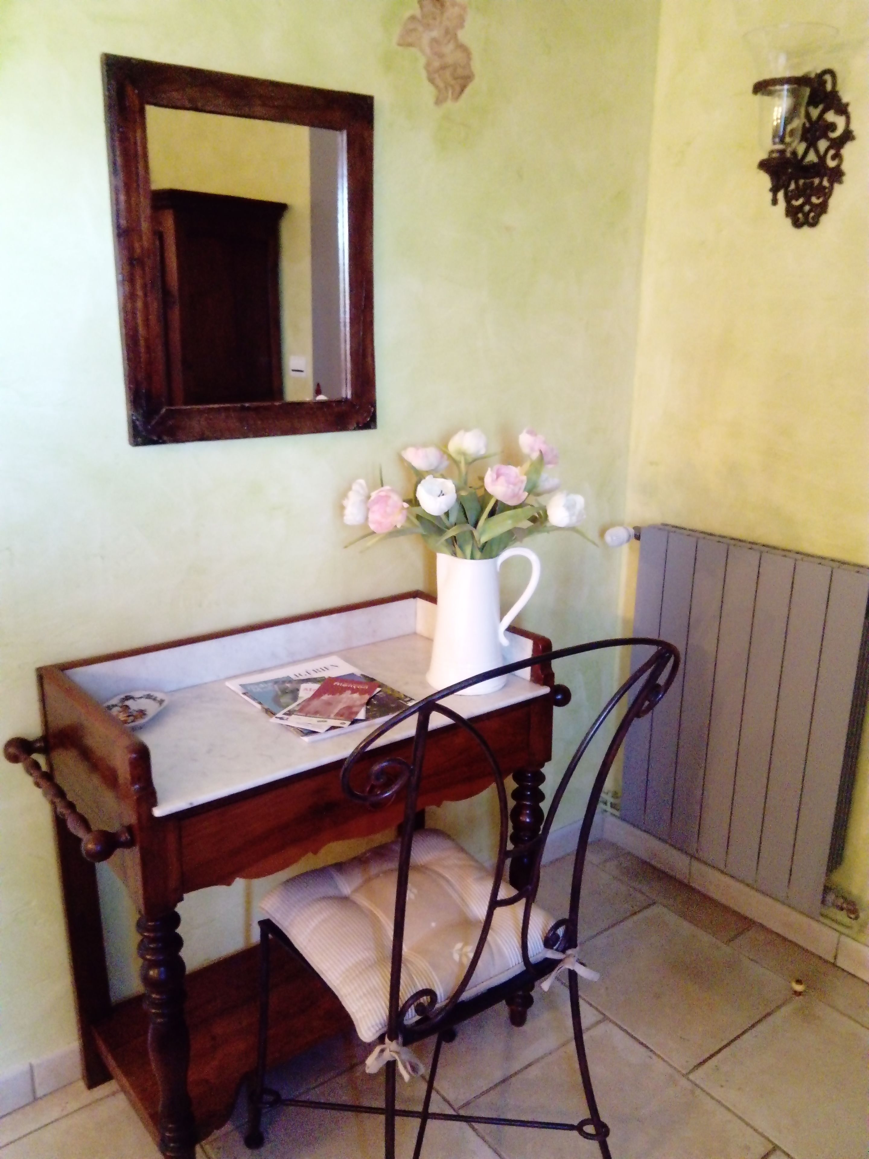 Un escritorio de madera con una taza blanca, una silla con cojín, un espejo y una lámpara de pared.