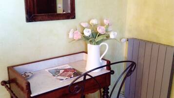 Un escritorio de madera con una taza blanca, una silla con cojín, un espejo y una lámpara de pared.