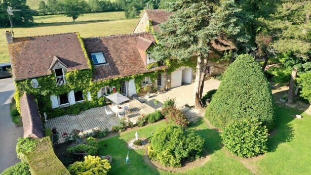 Une maison à deux étages avec une façade en briques, un toit en tuiles et une allée pavée menant à un patio couvert.