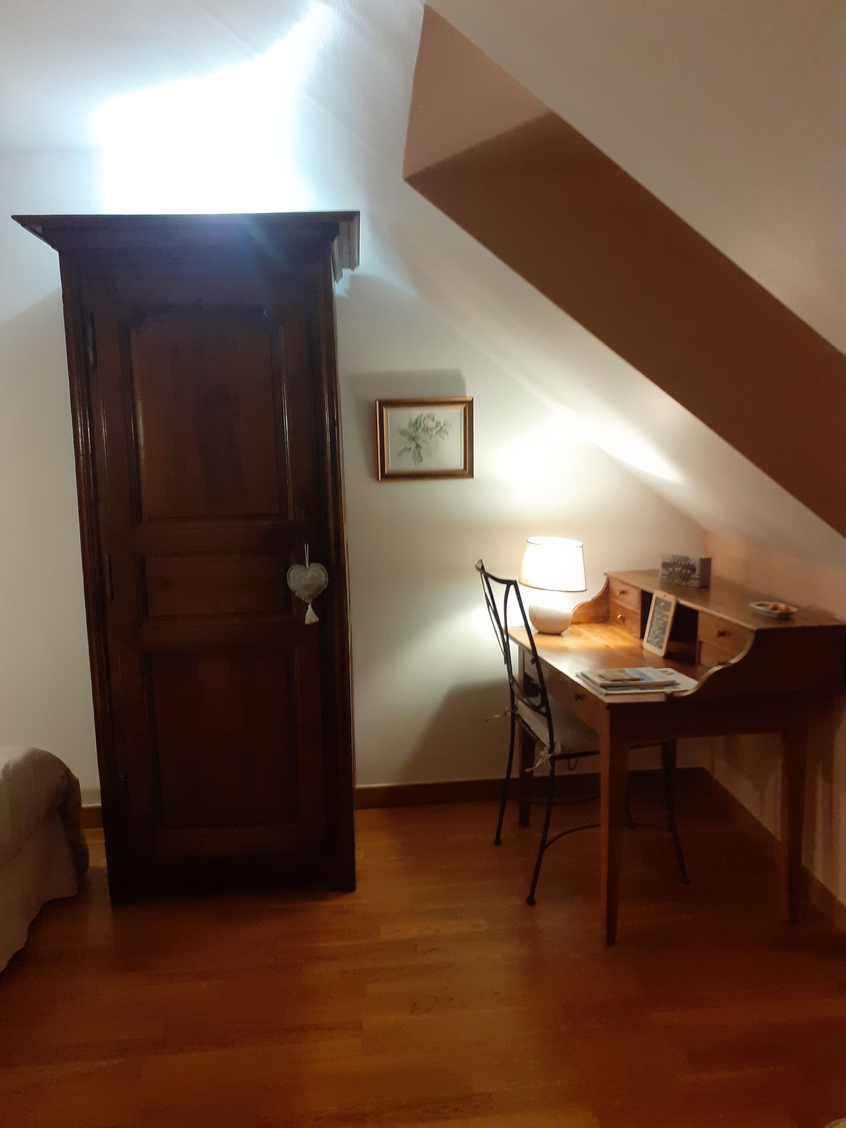 Une pièce avec une porte en bois, un bureau avec une chaise, une lampe et un tableau encadré au mur.