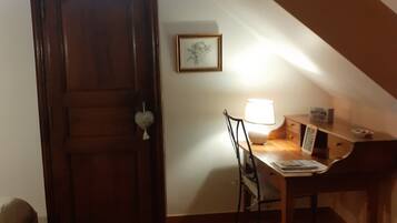 Une pièce avec une porte en bois, un bureau avec une chaise, une lampe et un tableau encadré au mur.