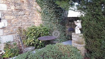 Een stenen muur begroeid met klimop, een tafeltje en een standbeeld in een tuin.