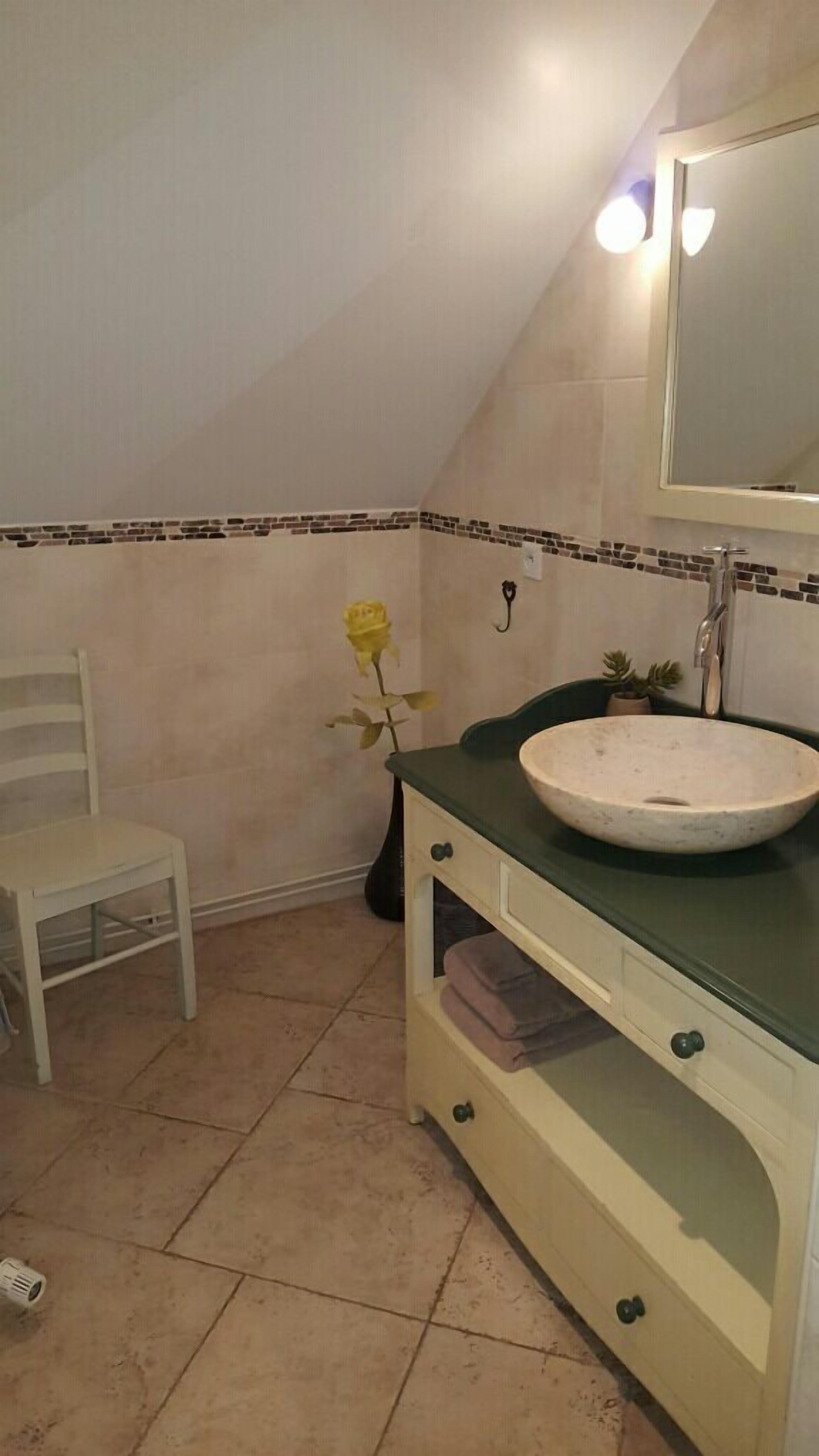 Een badkamer met een wit wastafelmeubel, een spiegel, een stoel en een potplant.
