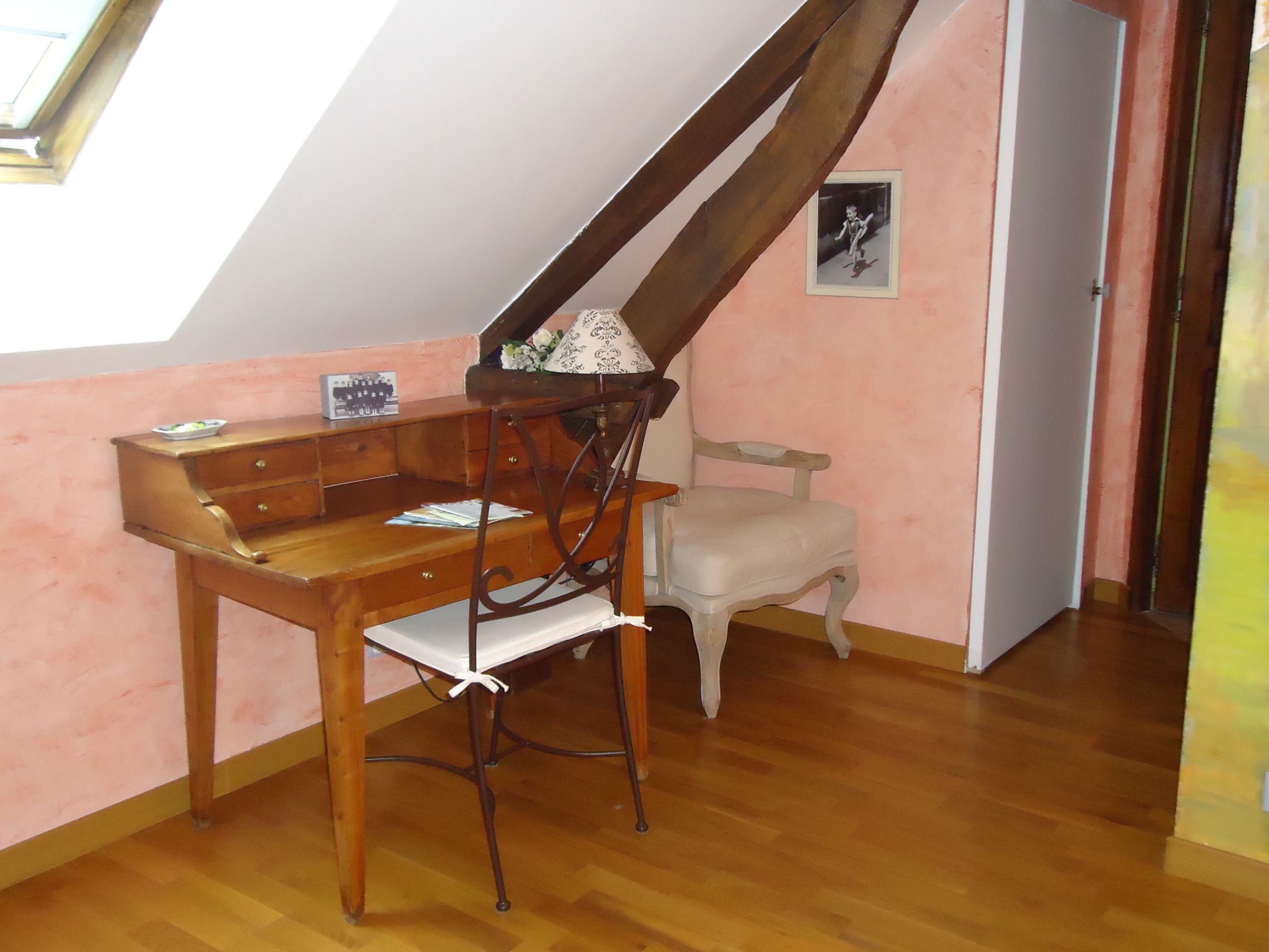 A room with a wooden desk, a chair, a small table, and a picture on the wall.