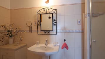 A bathroom with a white sink, a mirror with a decorative frame, a towel rack with a pink towel, and a potted plant with flowers.