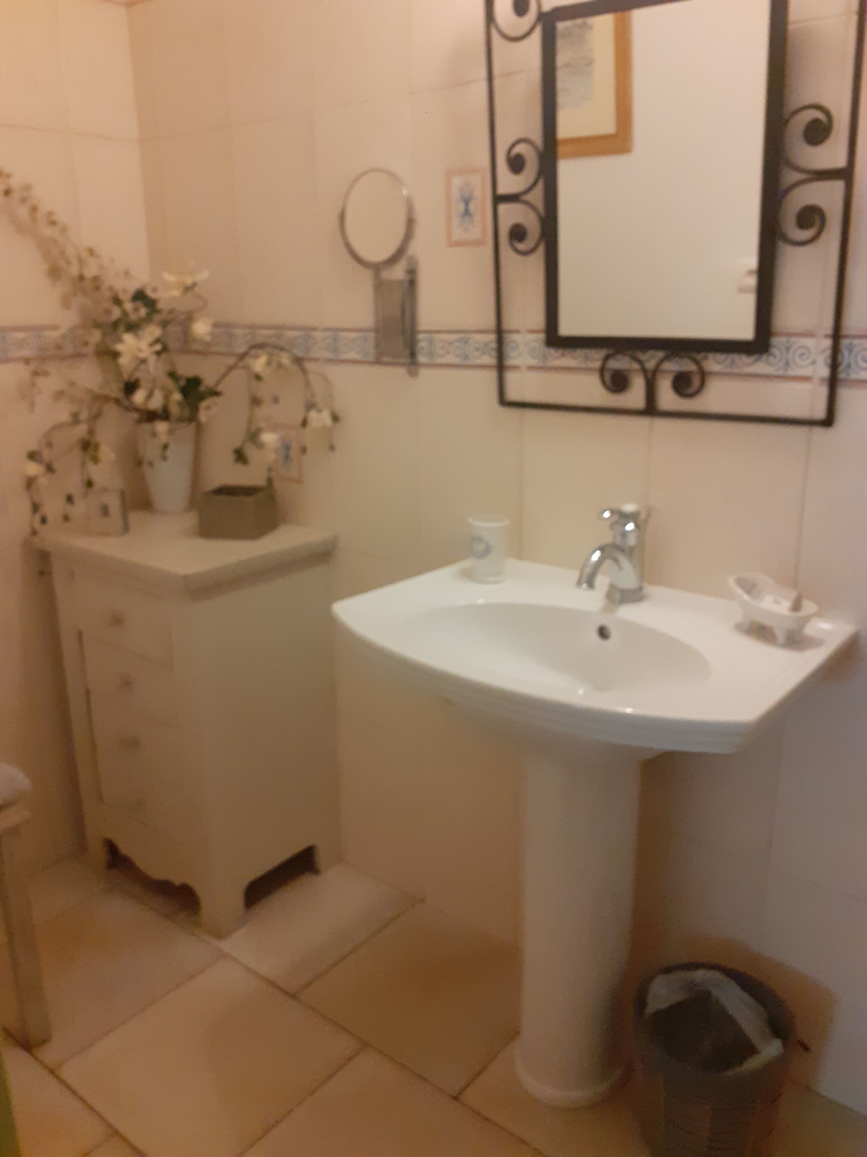 Un baño con lavamanos blanco, espejo y cubo de basura.