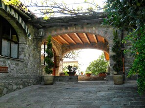 An arched stone gateway with wooden beams, leading to a building with a tiled roof. - Fattoria Giunasco (Bagnone)