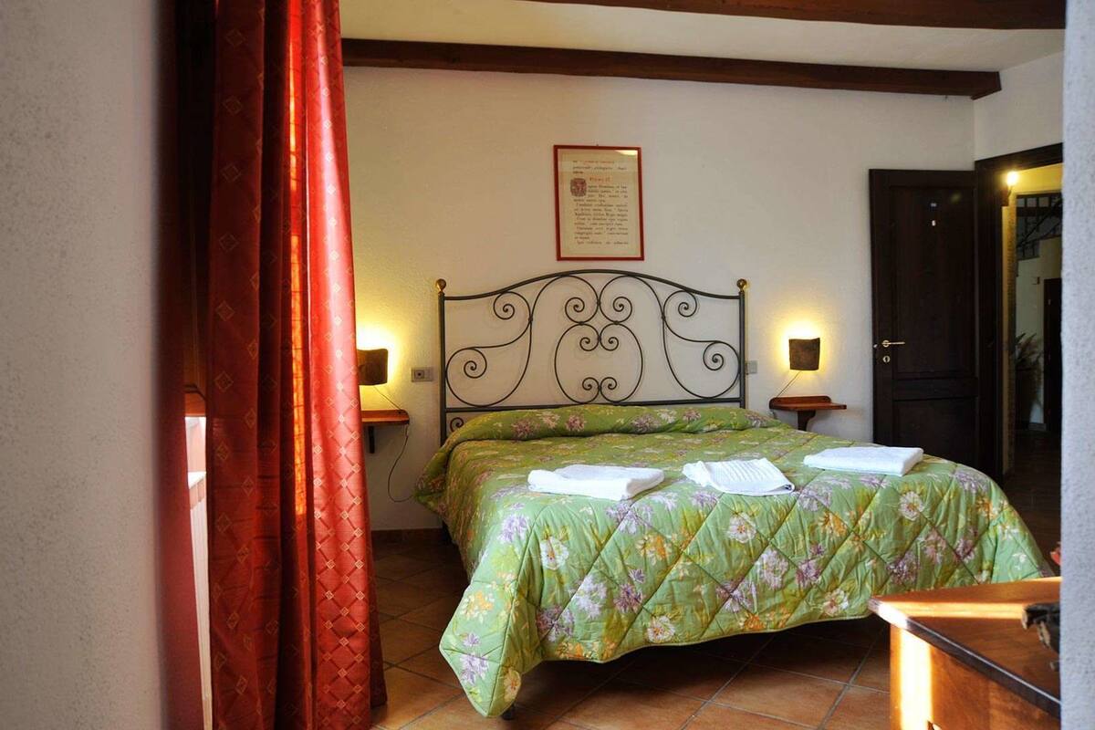 A bedroom with a bed, a nightstand, a wall-mounted lamp, and a door.