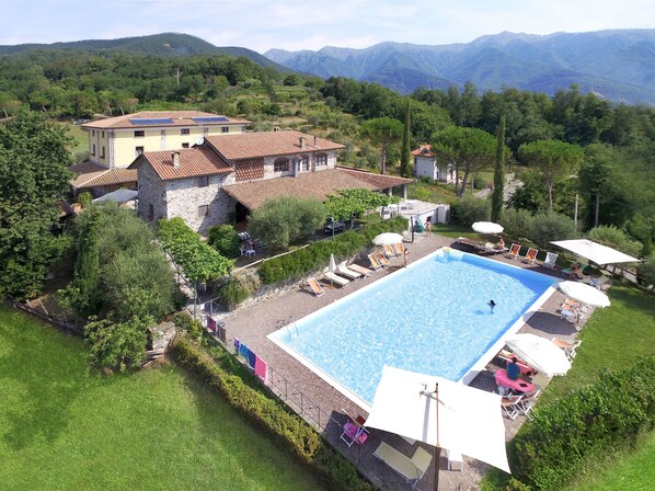 A large swimming pool with sun loungers and umbrellas, surrounded by lush greenery and a mountainous backdrop. - Fattoria Giunasco (Bagnone)