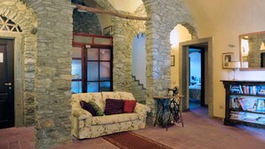 Una habitación con paredes de piedra, un sofá floral, una máquina de coser y una estantería.