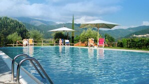 Una piscina con sillas de descanso y sombrillas, rodeada de vegetación y montañas.